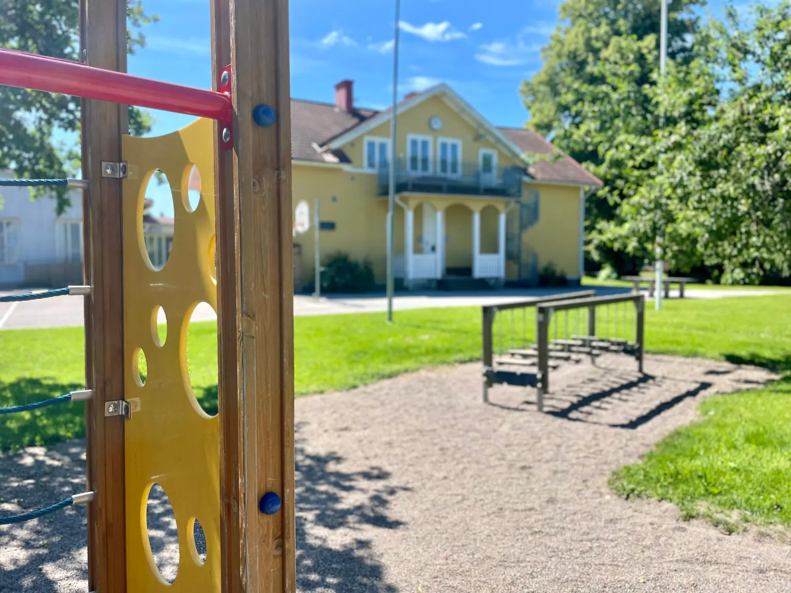 Skolgård med lekställning framför en gul skolbyggnad i Trosa kommun